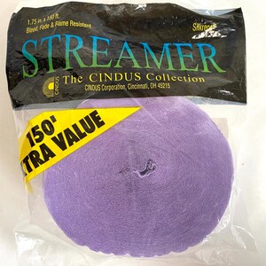 May include: A roll of lavender streamer paper in a clear plastic package. The package has a black top with the word "STREAMER" in green and blue letters. A yellow tag reads "150' EXTRA VALUE". The streamer is 1.75 inches wide and 150 feet long.
