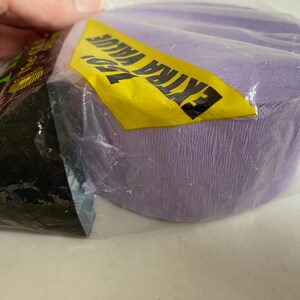 May include: A roll of lavender crepe paper is partially visible inside a clear plastic package. A yellow label with the words "EXTRA VALUE" in black is attached to the package. The paper has a textured surface.
