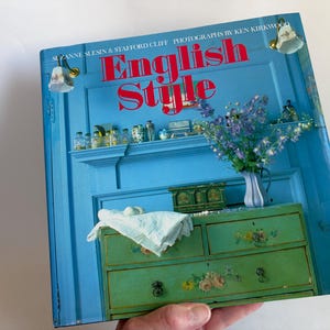 May include: A hardcover book titled English Style by Suzanne Slesin and Stafford Cliff with photographs by Ken Kirkwood. The cover features a bright blue wall, a green painted chest of drawers with floral details, and a vase of purple flowers.