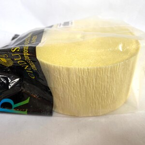 May include: A roll of light yellow crepe paper, partially visible within a clear plastic wrapper. The paper has a textured, crinkled surface. The packaging includes black and white text with the brand name "Cindus".