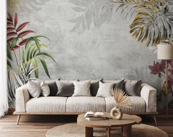 May include: A light beige sofa with pillows sits in front of a gray wall with a tropical leaf pattern. A wooden coffee table with a book and a vase with a dried plant sits in front of the sofa. A woven rug is on the floor.