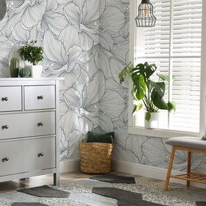 Peut inclure: Une commode grise &agrave; quatre tiroirs et des boutons noirs se trouve dans une pi&egrave;ce avec un mur blanc orn&eacute; d'un papier peint &agrave; motifs floraux. Une plante en pot est pos&eacute;e sur la commode. Un panier en osier se trouve sur le sol &agrave; c&ocirc;t&eacute; d'un banc gris avec un coussin et un oreiller &agrave; motifs noir et blanc.