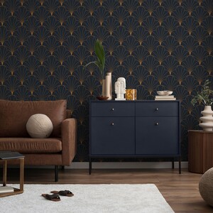 K&ouml;nnte beinhalten: Eine dunkelblaue Tapete mit einem goldenen geometrischen Muster aus &uuml;berlappenden F&auml;cherformen. Vor der Tapete steht ein braunes Ledersofa mit einem Holz-Beistelltisch und einem Buch darauf. Rechts vom Sofa steht ein dunkelblauer Schrank mit zwei Schubladen und zwei T&uuml;ren. Rechts vom Schrank steht ein Holz-Beistelltisch mit einer beigefarbenen Vase und einem beigefarbenen Ottoman.