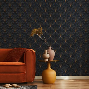 K&ouml;nnte beinhalten: Ein Wohnzimmer mit einem orangefarbenen Sofa und einem Beistelltisch mit zwei Vasen und getrockneten Blumen. Die Wand ist mit dunkelblauem Tapetenpapier mit einem goldenen geometrischen Muster bedeckt.