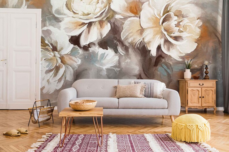 May include: A living room interior with a gray sofa, a wooden coffee table, a wooden cabinet, and a yellow knitted pouf. The wall behind the sofa is decorated with a large floral mural featuring white and brown peonies.