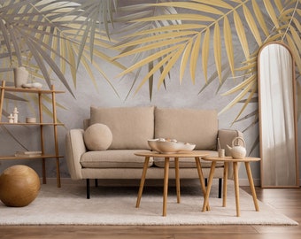 May include: A living room interior with a beige sofa, two wooden coffee tables, a wooden shelf, and a large mirror. The wall behind the sofa is decorated with a wallpaper featuring a pattern of gold and gray palm leaves.