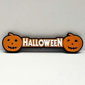 May include: Orange Halloween banner with two jack-o'-lantern faces on either end and the word "HALLOWEEN" in white letters.