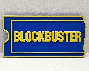 May include: A blue and yellow plastic replica of a Blockbuster Video ticket stub. The ticket stub has the word "BLOCKBUSTER" printed in yellow letters.