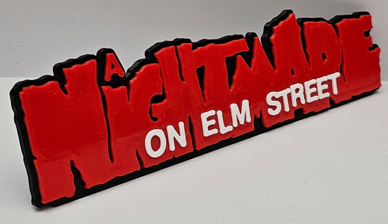 Op de afbeelding: Een "A Nightmare on Elm Street" logo, rood met zwarte omtrek, op een witte achtergrond. De tekst is in een vet, gestileerd lettertype.