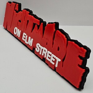 Op de afbeelding: Een "A Nightmare on Elm Street" logo, 3D-geprint in rood met een zwarte omtrek en witte letters.