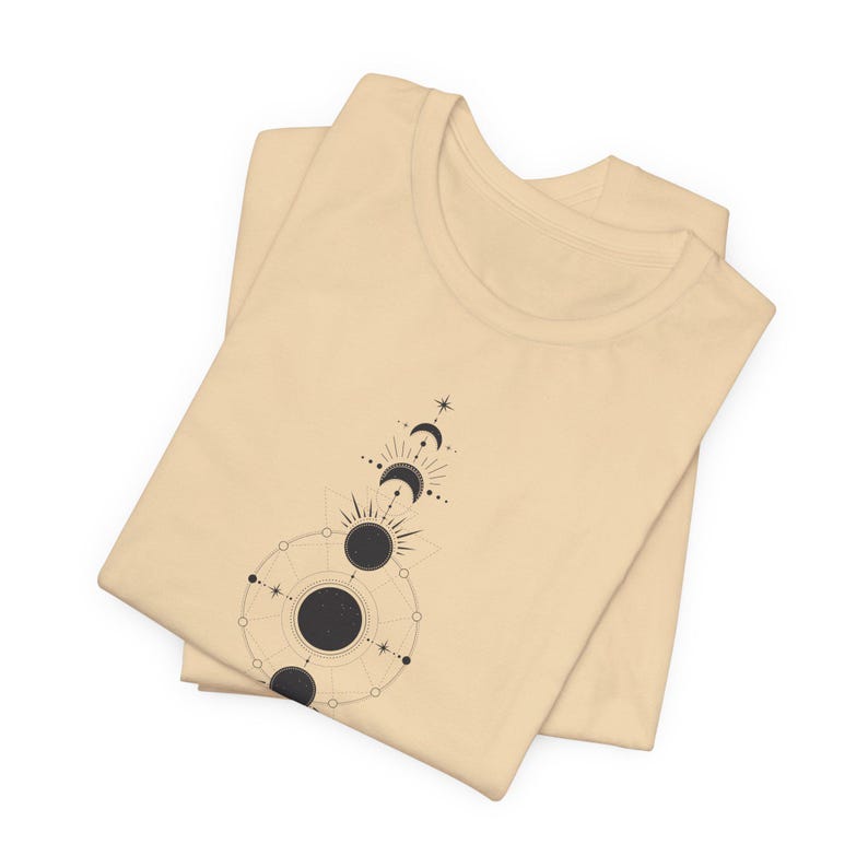 May include: A beige t-shirt featuring a black and white graphic of a celestial design with moons and stars.