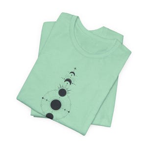 May include: A light green t-shirt featuring a black and white geometric design of a crescent moon and sun.