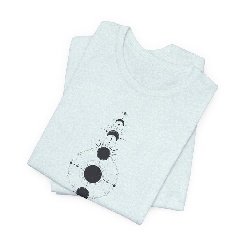 May include: A light grey t-shirt featuring a black and white graphic design of celestial moon and sun phases with geometric shapes.