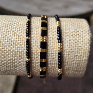May include: Three beaded bracelets, one with black and gold square beads, and two with black and gold round beads.