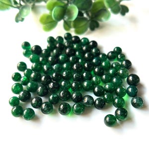 以下が含まれることがあります： ジュエリー作りに使える、濃い緑色の丸いビーズの山。おそらく翡翠かアベンチュリン製です。