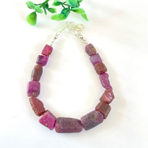 May include: A pink and red gemstone bracelet with silver clasps. The bracelet is made of rough, irregular shaped stones.
