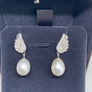 May include: A pair of silver earrings with a pearl drop and a wing design with clear cubic zirconia stones.