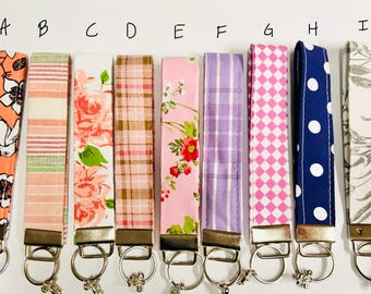 May include: Nine fabric key fobs with various patterns, including floral, plaid, and polka dots. Colors range from coral and pink to blue and lavender. Each fob has a metal clasp and key ring.