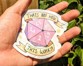 May include: A pink and purple iridescent sticker with a dice and the text "That's not how this works!"