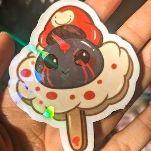 May include: A sticker of a cartoon character with a red mushroom cap, black eyes, and a white body with red dots. The character is holding a brown popsicle stick.