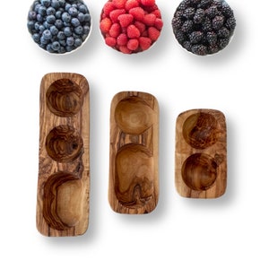 Puede incluir: Tres cuencos de servir de madera en diferentes tamaños y formas. Los cuencos están hechos de madera de olivo y tienen un acabado natural. Los cuencos son perfectos para servir aperitivos, salsas o entrantes.