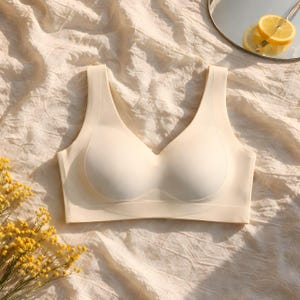 May include: A seamless, cream-colored sports bra with a V-neck design. The bra has molded cups and wide straps. The image is taken on a cream-colored, textured fabric, with yellow flowers and a mirror with lemon slices in the background.