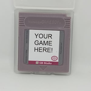 May include: A purple Game Boy cartridge with a white label that says "YOUR GAME HERE!" and "GB Studio". The cartridge is in a clear plastic case.