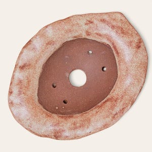 May include: A handmade ceramic planter with an irregular, organic shape. The planter is glazed in a light brown color with a speckled texture. It has a circular opening in the center and several drainage holes around the rim.