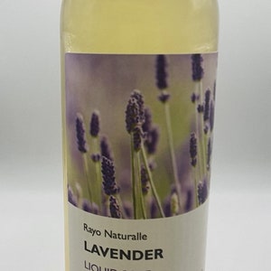 May include: A clear bottle of Rayo Naturalle Lavender Liquid Soap. The label features a lavender field illustration. The bottle has a black cap and contains a yellow liquid. Net weight is 16oz.