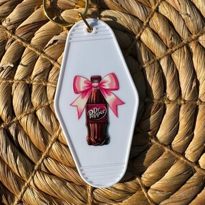 May include: White motel key chain with a Dr Pepper bottle with a pink bow.