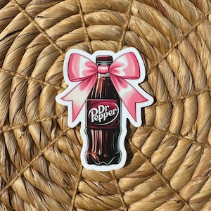May include: A sticker of a Dr Pepper bottle with a pink bow on top. The bottle is brown and the bow is pink with white accents.