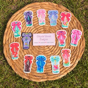 May include: A collection of twelve colorful energy drink stickers, each featuring a prominent decorative bow at the top. A rectangular white card in the center displays the text Chiquis' Sweet Designs, Stationery, Accessories, Custom Requests.