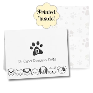 May include: White folded card with a black paw print and the letter "D" inside. The text "Dr. Cyndi Davidson, DVM" is below the paw print. A row of cartoon pet faces is at the bottom. The words "Printed Inside!" are on a yellow flower-shaped tag.