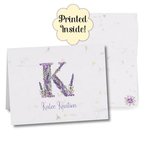 Puede incluir: Una tarjeta de felicitación plegada blanca con un diseño floral de lavanda "K" y el nombre "Kalee Knutson" en escritura púrpura. La tarjeta tiene un patrón floral y el texto "Printed Inside!" en una nube.