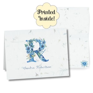 Puede incluir: Tarjeta de papelería plegada con una 'R' floral azul y el nombre 'Sandra Robertson'. El fondo blanco texturizado presenta un diseño floral a juego. Una etiqueta amarilla dice 'Printed Inside!'