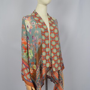 May include: A patterned kimono-style garment with a floral and geometric design in shades of teal, orange, red, and blue. The fabric drapes over a mannequin, showcasing the flowing design and vibrant colours. The garment is a stylish addition to any wardrobe.