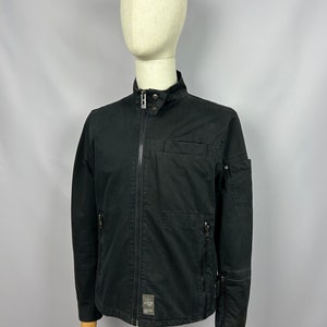 May include: A black zip-up jacket with a stand-up collar and multiple pockets. The jacket has a G-Star RAW logo patch on the left side.