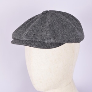 May include: A gray newsboy cap with a rounded crown and a short, stiff brim. The cap is made of a textured fabric and is displayed on a mannequin head against a white background. This classic style is suitable for various outfits.