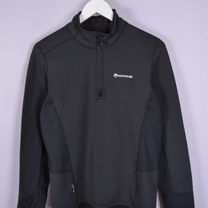 May include: Black athletic long-sleeve shirt with a quarter-zip closure and the brand name "MONTANE" in white. The shirt has a high collar and is hanging on a white hanger.