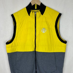 Puede incluir: Un chaleco acolchado sin mangas amarillo y gris con una cremallera negra y ribetes negros. El chaleco tiene un logotipo en la parte delantera que dice "Polo" y presenta un peque&ntilde;o logotipo con un caballo y un jinete.