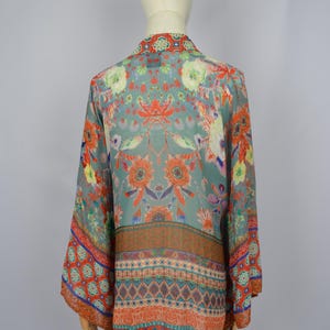 May include: A patterned kimono-style top in teal, with floral and geometric designs in orange, red, and blue. The sleeves are wide, and the fabric appears lightweight. The garment is displayed on a mannequin.