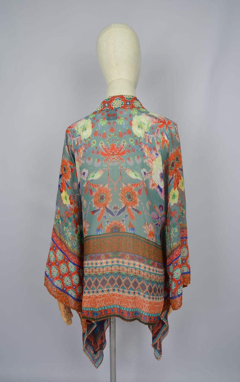 May include: A patterned kimono-style top in teal, with floral and geometric designs in orange, red, and blue. The sleeves are wide, and the fabric appears lightweight. The garment is displayed on a mannequin.