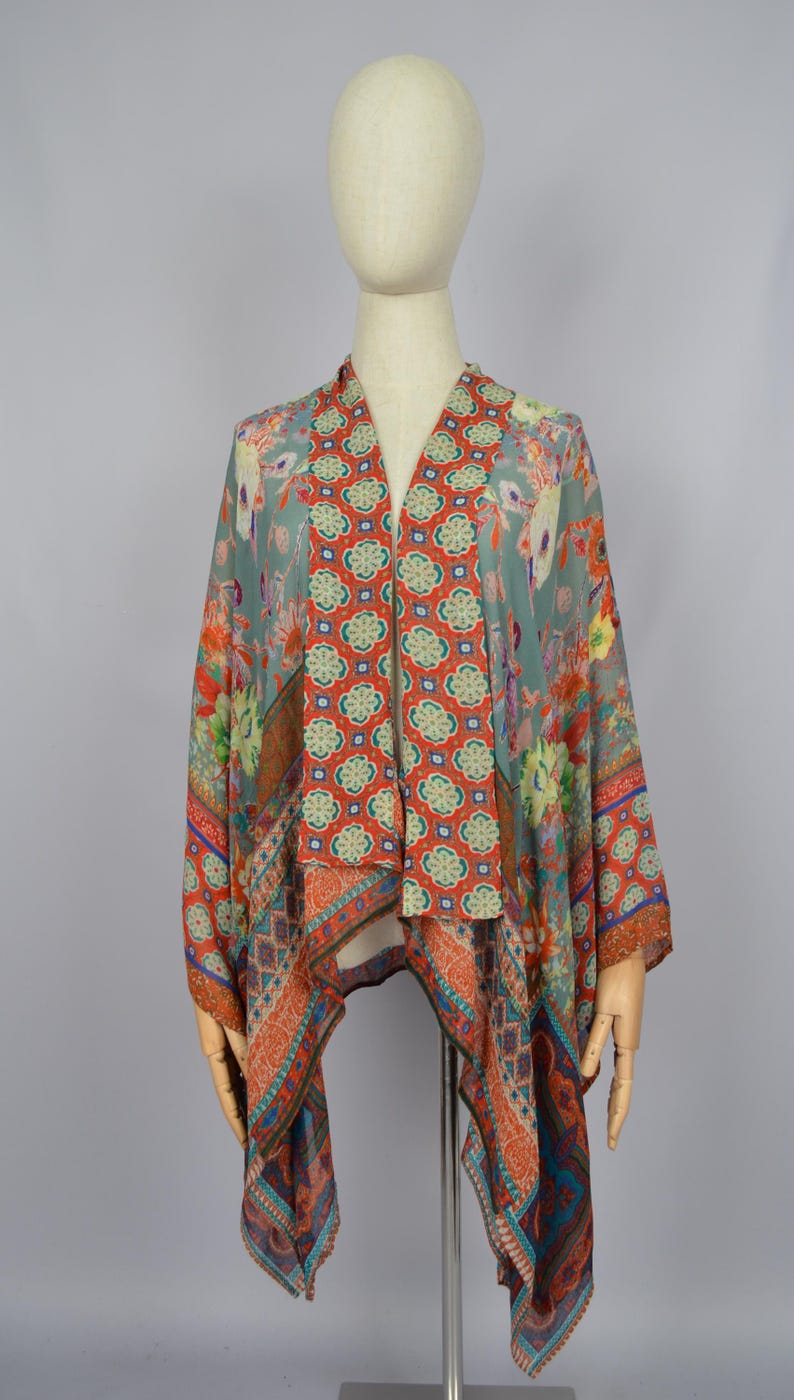 May include: A patterned kimono-style top with a V-neck. The fabric features floral and geometric designs in shades of orange, blue, and green. The garment is displayed on a mannequin.