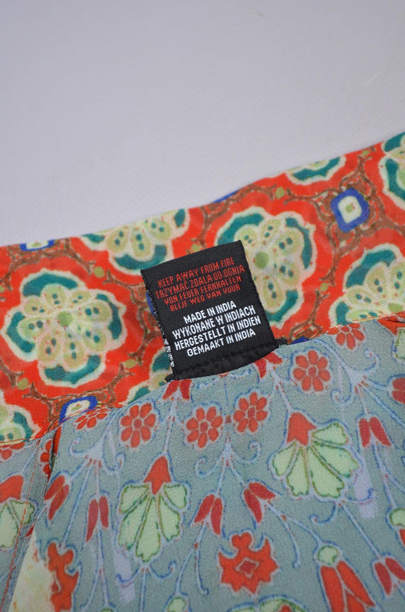 May include: Close-up of a patterned fabric with a tag. The fabric features a red and teal floral design. The tag reads "KEEP AWAY FROM FIRE" in multiple languages, and "MADE IN INDIA".