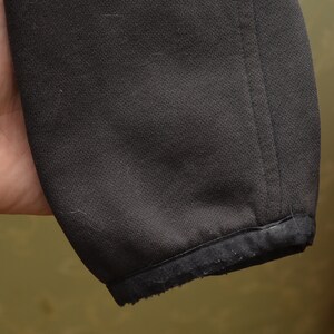 May include: Close-up of the black fabric cuff of a jacket. The cuff is made of a soft, stretchy material and has a slightly frayed edge.