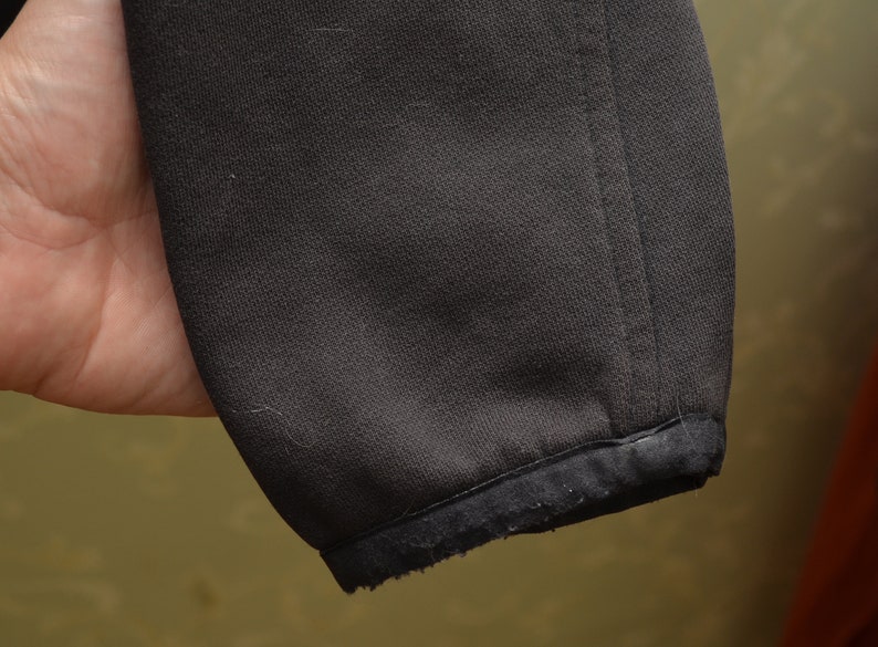 May include: Close-up of the black fabric cuff of a jacket. The cuff is made of a soft, stretchy material and has a slightly frayed edge.