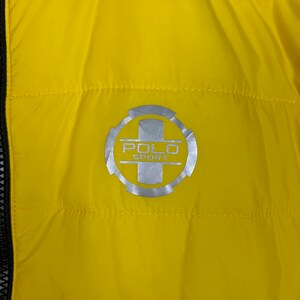 Puede incluir: Chaqueta acolchada amarilla con un logotipo Polo Sport plateado en el pecho.