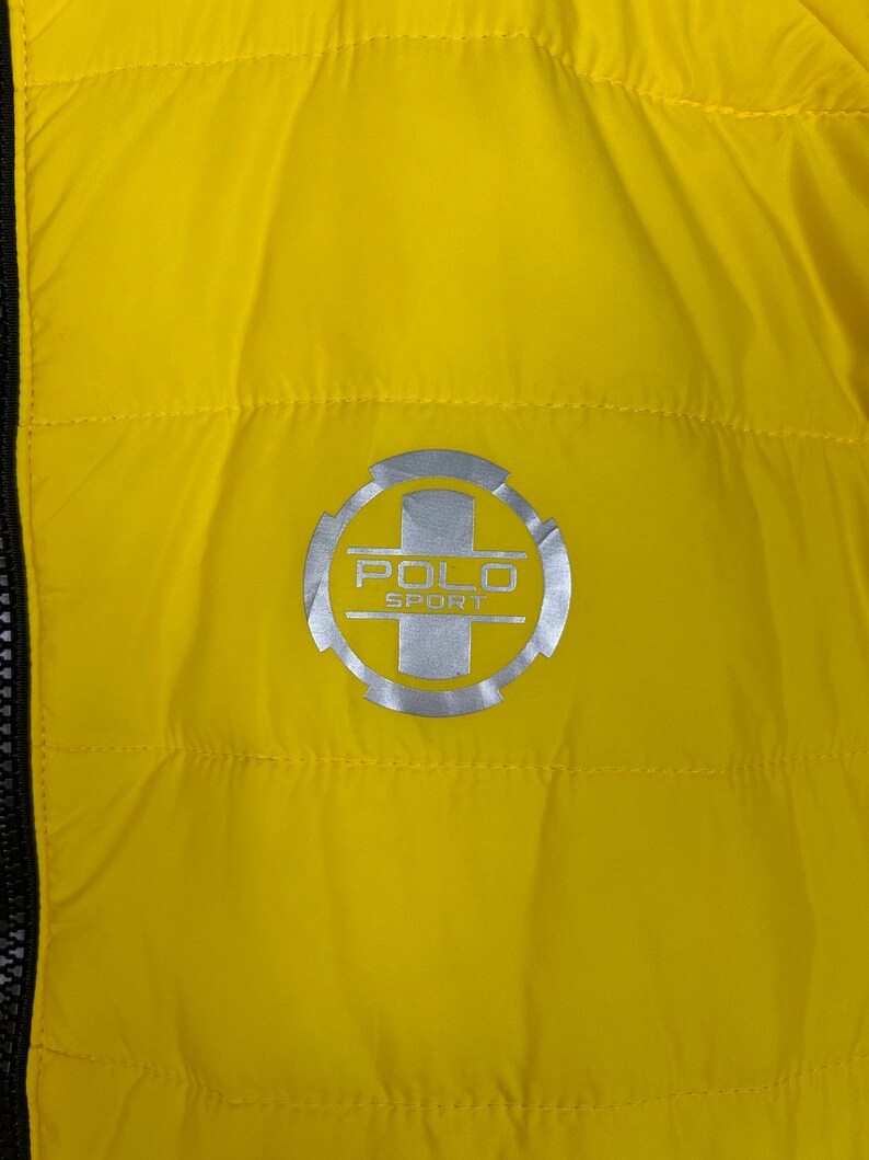 Puede incluir: Chaqueta acolchada amarilla con un logotipo Polo Sport plateado en el pecho.
