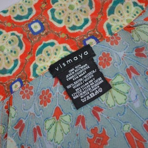 May include: A patterned fabric with a floral design in red, green, and blue. The fabric has a label that reads "vismaya" and includes care instructions. The fabric is made of 100% rayon.
