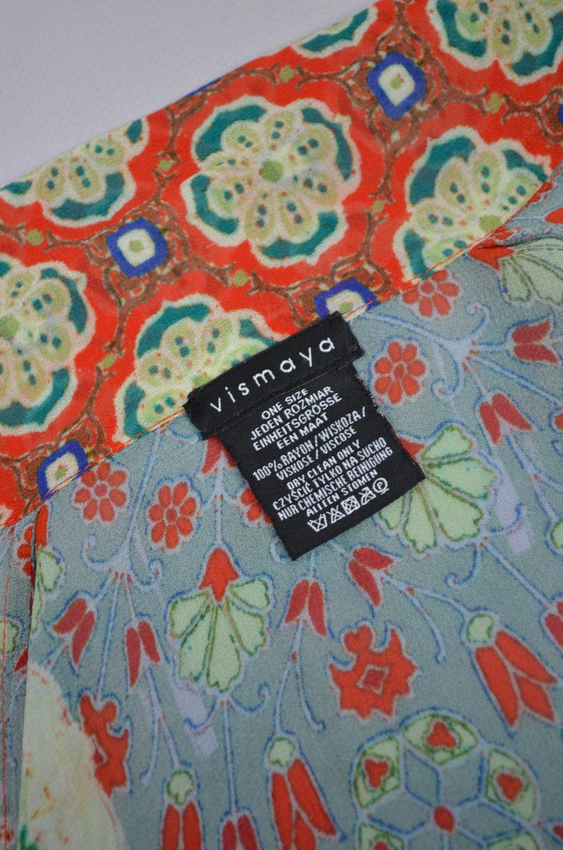 May include: A patterned fabric with a floral design in red, green, and blue. The fabric has a label that reads "vismaya" and includes care instructions. The fabric is made of 100% rayon.